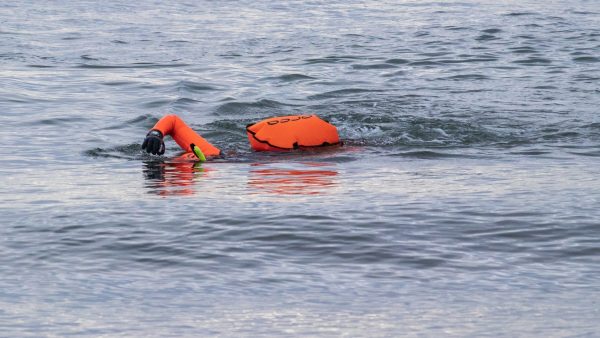 A swimmer in a lake with an orange wetsuit and tow float